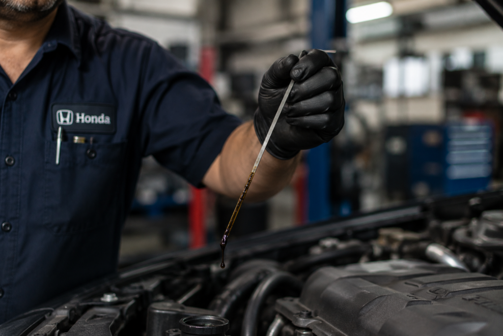 Mechanic checking dark oil on dipstick, showing Signs Your Honda Accord Needs an Oil Change Now before engine damage occurs.